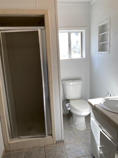 bathroom with a stall shower, toilet, vanity, tile patterned floors, and crown molding