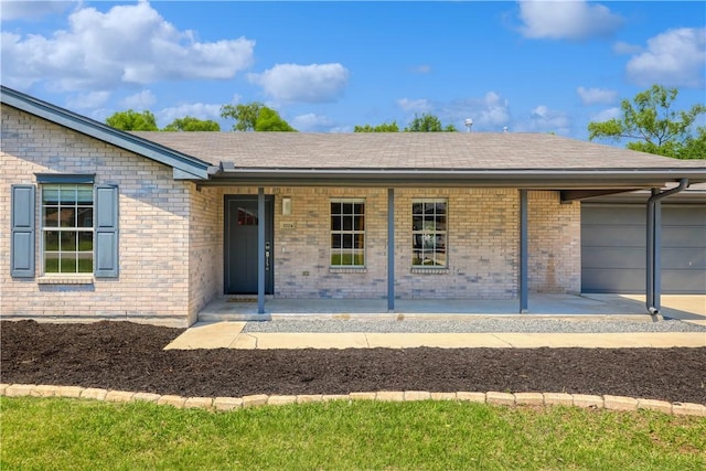 doorway to property with covered porch, a shingled roof, a garage, and brick siding