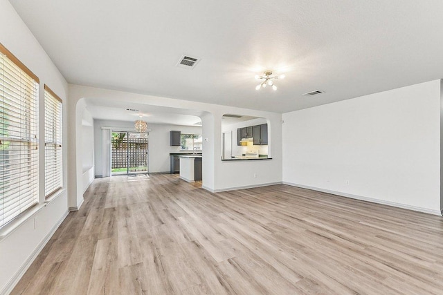 1208 Water Spaniel Way, Round Rock, TX 78664 - unfurnished living room featuring a chandelier, light wood finished floors, arched walkways, and baseboards