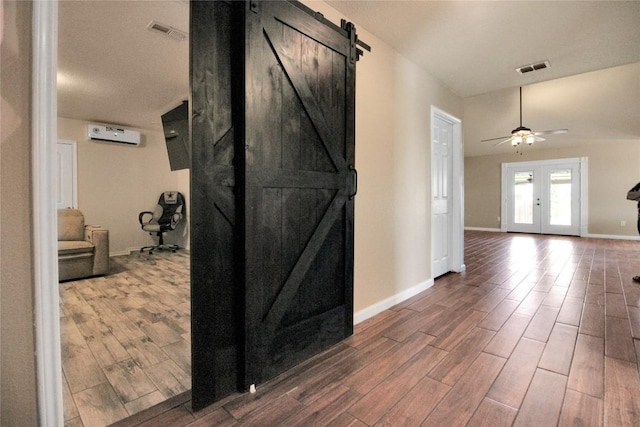 corridor featuring wood finished floors, a barn door, baseboards, and french doors