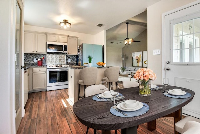 kitchen with stainless steel appliances, wood finished floors, tasteful backsplash, dark countertops, and lofted ceiling