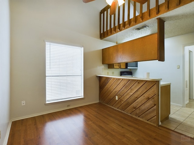 2210 Pearl St Unit 306, Austin, TX 78705 - kitchen with light wood finished floors, a ceiling fan, brown cabinets, baseboards, and a high ceiling