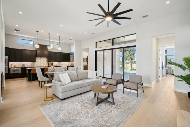 living room with healthy amount of natural light, recessed lighting, light wood-style floors, ceiling fan, and a high ceiling