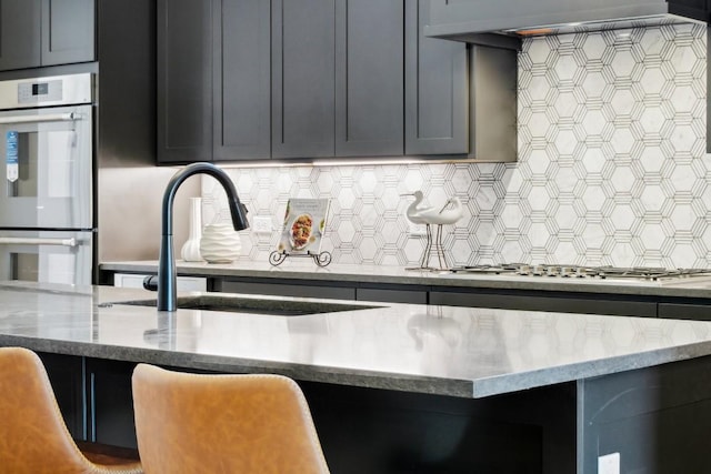 kitchen with a sink, appliances with stainless steel finishes, backsplash, and light stone countertops
