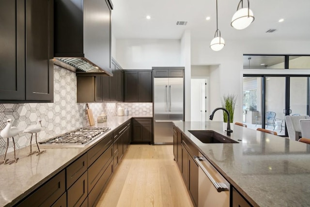 kitchen featuring a sink, wall chimney exhaust hood, stainless steel appliances, dark stone counters, and light wood-style flooring