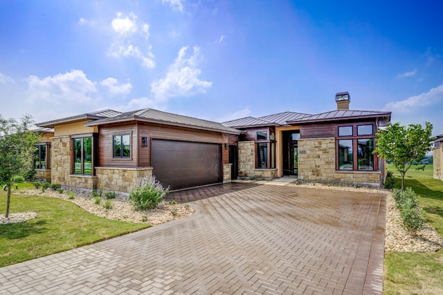 prairie-style house featuring stone siding, a chimney, a garage, and a standing seam roof