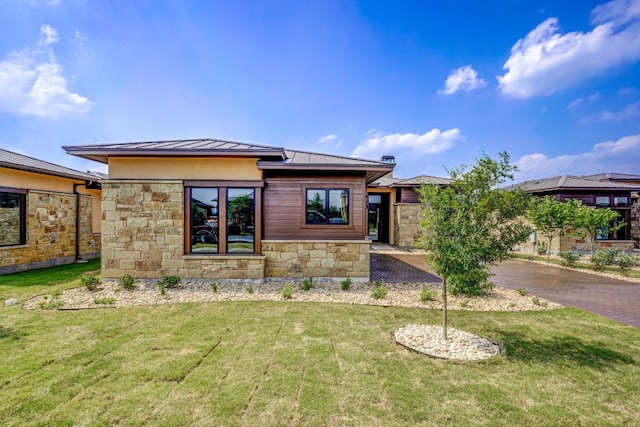 prairie-style house with a standing seam roof, stone siding, metal roof, and a front lawn
