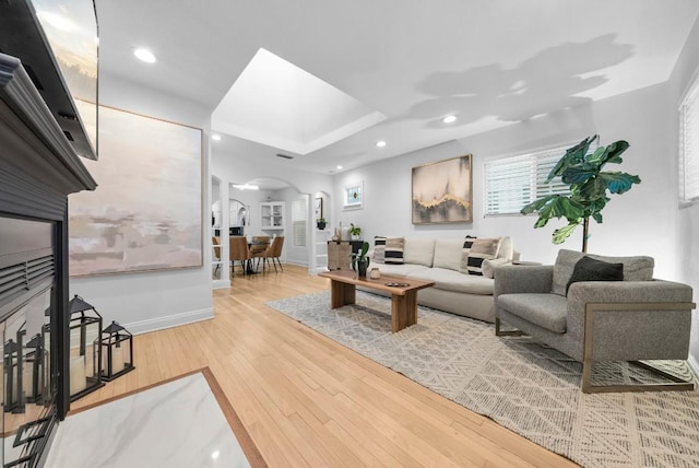 living room featuring arched walkways, wood finished floors, baseboards, a tray ceiling, and recessed lighting