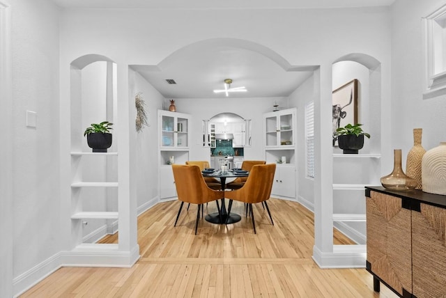 dining room featuring wood-type flooring, arched walkways, and baseboards