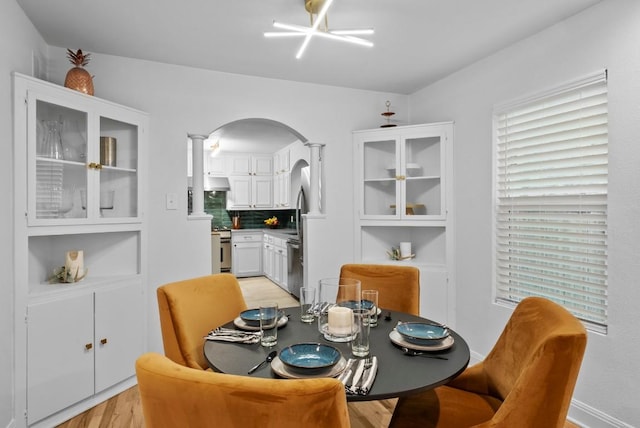 dining area with arched walkways, light wood-type flooring, and decorative columns