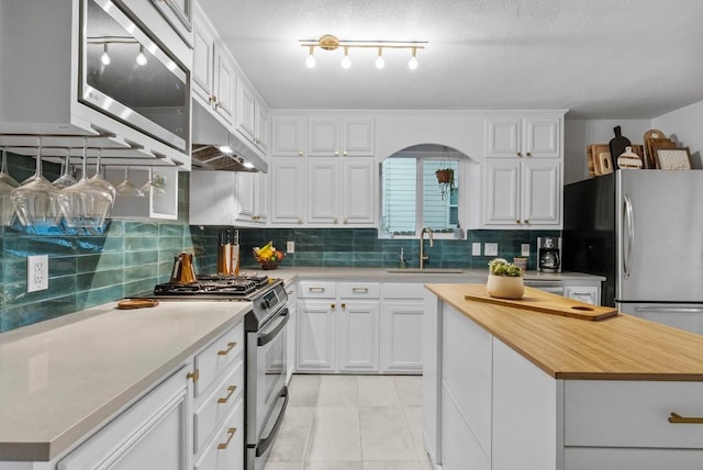 kitchen with under cabinet range hood, stainless steel appliances, a sink, wooden counters, and white cabinetry