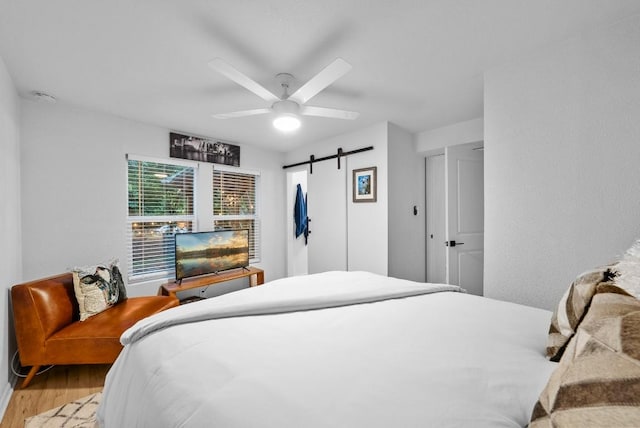 bedroom with wood finished floors, a barn door, and a ceiling fan
