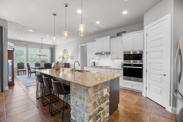128 Tuscany Way, Georgetown, TX 78633 - kitchen featuring stainless steel appliances, a sink, under cabinet range hood, tasteful backsplash, and light stone countertops