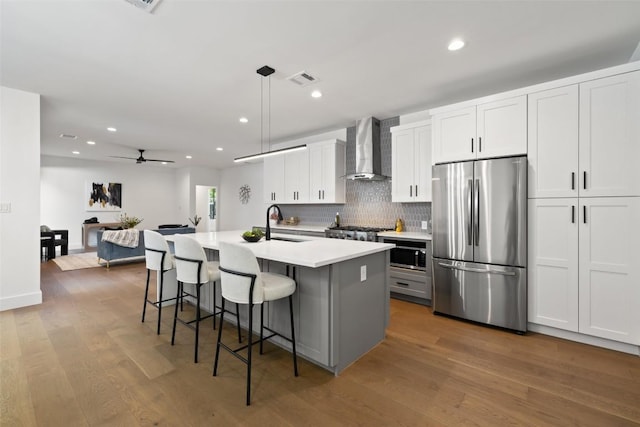 3705 Wilson St Unit 1, Austin, TX 78704 - kitchen featuring stainless steel appliances, wall chimney exhaust hood, an island with sink, tasteful backsplash, and wood finished floors