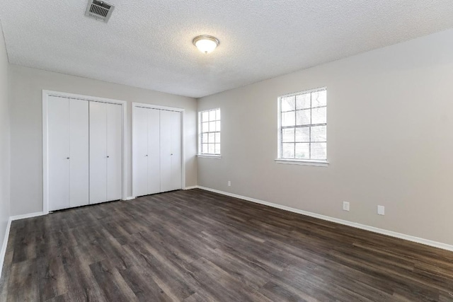 7301 Scenic Brook Dr, Austin, TX 78736 - unfurnished bedroom with two closets, dark wood-style floors, baseboards, and a textured ceiling