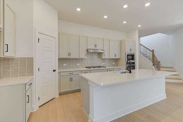 1352 S Brook Dr, Leander, TX 78641 - kitchen featuring a sink, light wood-style flooring, stainless steel appliances, under cabinet range hood, and a center island with sink