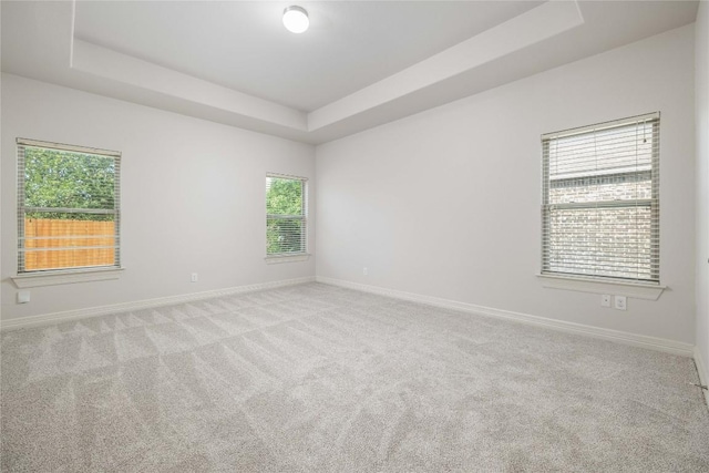carpeted empty room with a tray ceiling and baseboards
