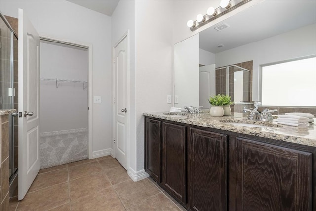 full bath with a stall shower, a walk in closet, tile patterned floors, double vanity, and baseboards