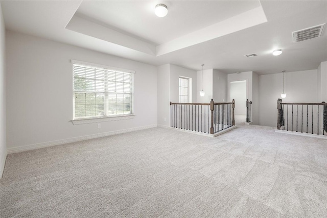 carpeted empty room featuring a raised ceiling, plenty of natural light, and baseboards