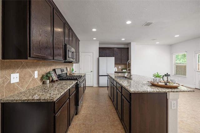 kitchen featuring appliances with stainless steel finishes, a sink, dark brown cabinetry, decorative backsplash, and recessed lighting