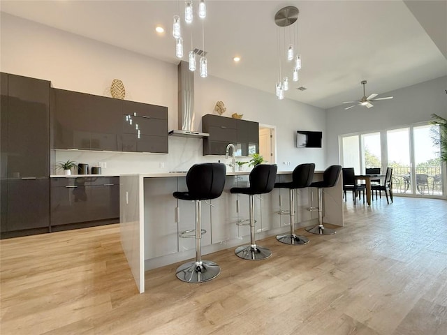 kitchen featuring modern cabinets, a breakfast bar area, light wood-style floors, a ceiling fan, and a towering ceiling