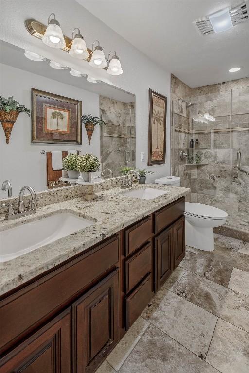 bathroom with toilet, a stall shower, and double vanity