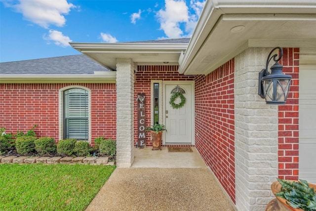 property entrance featuring roof with shingles and brick siding