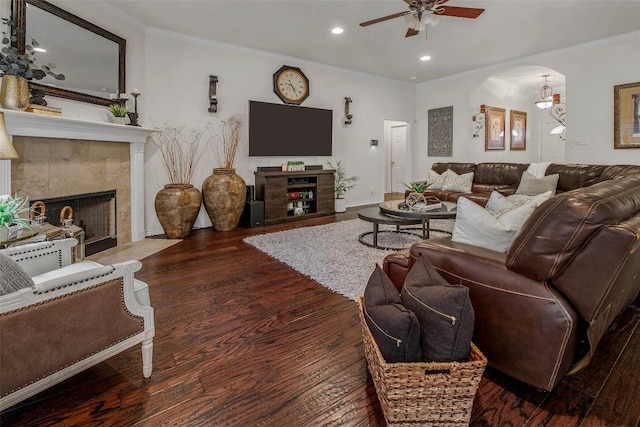 living room featuring a fireplace, a ceiling fan, ornamental molding, arched walkways, and wood finished floors