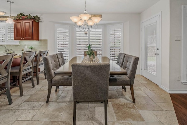 dining space featuring stone tile flooring, plenty of natural light, a chandelier, and baseboards