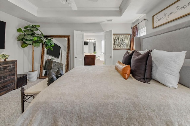 bedroom with a tray ceiling, crown molding, carpet floors, ensuite bathroom, and ceiling fan