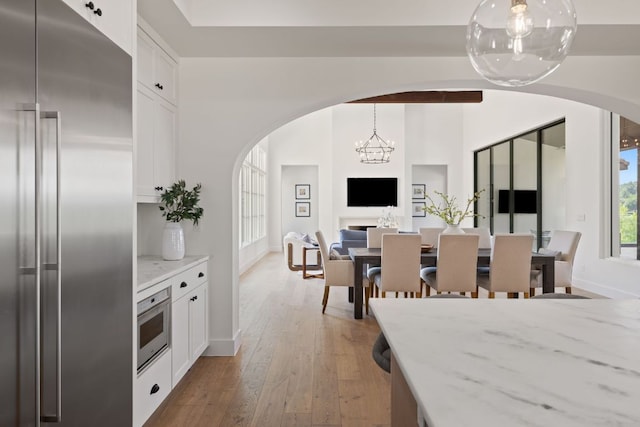 12625 Maidenhair Ln Unit 31, Austin, TX 78738 - kitchen with stainless steel appliances, arched walkways, white cabinets, light stone counters, and a chandelier