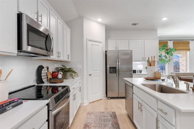 552 Tekoa Dr, Georgetown, TX 78628 - kitchen featuring stainless steel appliances, a sink, light wood finished floors, white cabinets, and backsplash