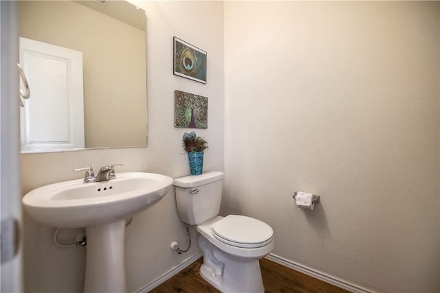 half bathroom featuring wood finished floors, baseboards, toilet, and a sink