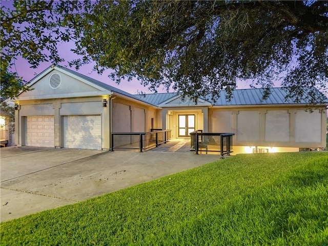 view of front of house featuring a standing seam roof, driveway, a yard, an attached garage, and metal roof