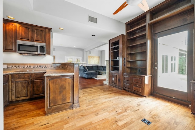 kitchen with stainless steel microwave, light wood finished floors, ceiling fan, black electric stovetop, and open floor plan