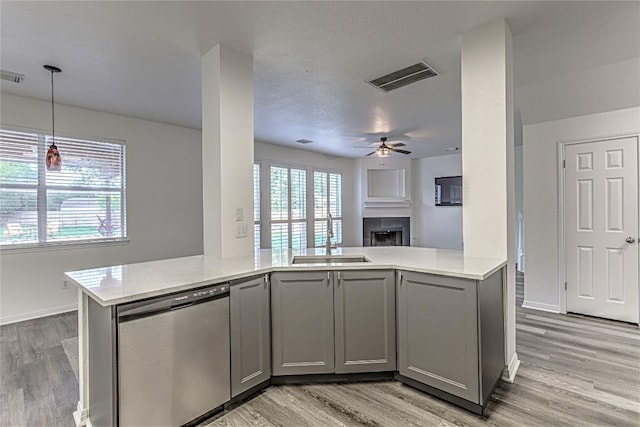 kitchen featuring stainless steel dishwasher, gray cabinets, a fireplace, a ceiling fan, and light wood finished floors