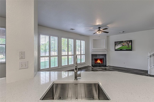 kitchen featuring a sink, a fireplace, a ceiling fan, light stone countertops, and open floor plan