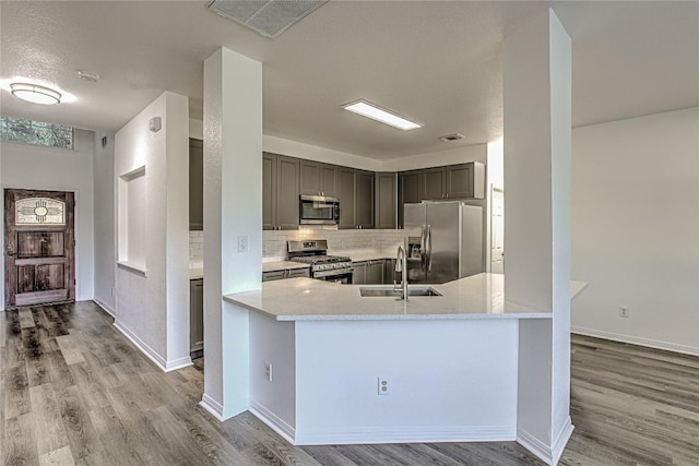 kitchen featuring appliances with stainless steel finishes, a sink, wood finished floors, tasteful backsplash, and gray cabinetry