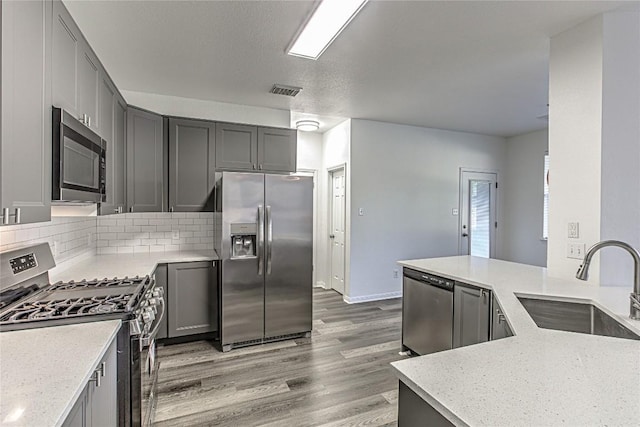 kitchen with stainless steel appliances, a sink, light wood-style floors, tasteful backsplash, and gray cabinets