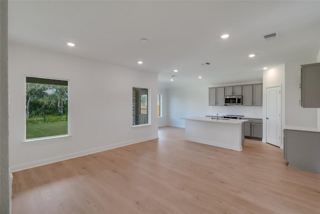 513 Tekoa Dr, Georgetown, TX 78628 - kitchen with stainless steel microwave, gray cabinets, light wood-type flooring, an island with sink, and recessed lighting