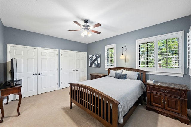 bedroom with multiple closets, light carpet, and a ceiling fan