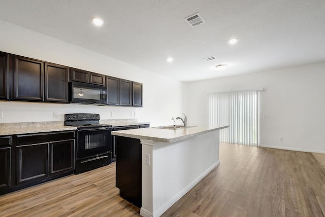 750 Bunton Reserve Blvd, Kyle, TX 78640 - kitchen with black appliances, light wood-style floors, light countertops, a kitchen island with sink, and recessed lighting