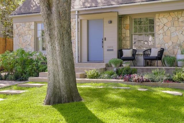 entrance to property featuring stone siding, a lawn, and a shingled roof