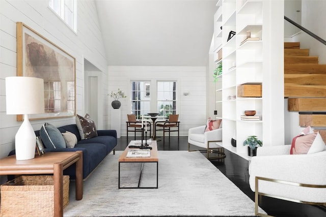living room featuring high vaulted ceiling, stairway, wooden walls, and wood finished floors
