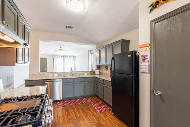 404 Paige Bnd, Hutto, TX 78634 - kitchen featuring appliances with stainless steel finishes, lofted ceiling, dark wood-style flooring, gray cabinets, and light stone countertops