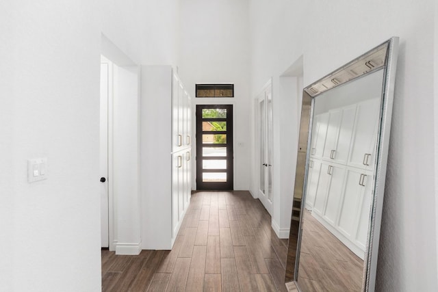 corridor with wood finished floors, baseboards, and a high ceiling