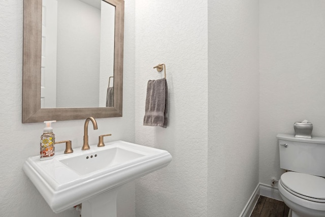 half bathroom featuring a sink, wood finished floors, toilet, baseboards, and a textured wall