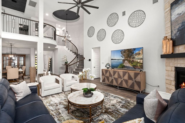 living area with a high ceiling, wood finished floors, ceiling fan, stairs, and a fireplace