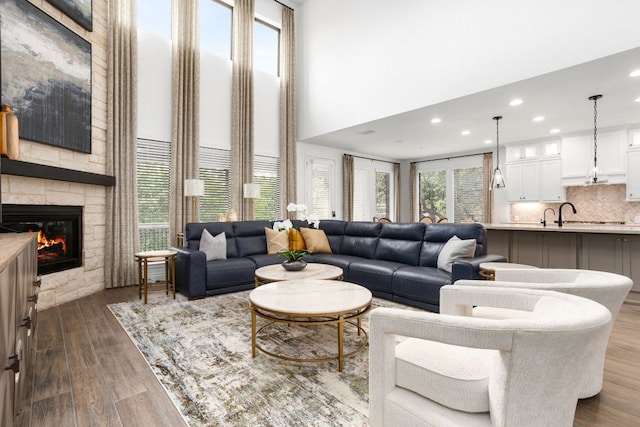 living area with a towering ceiling, a stone fireplace, dark wood-type flooring, and recessed lighting