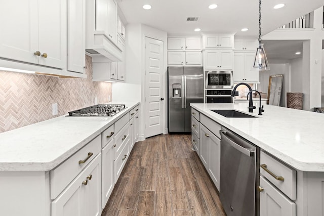 kitchen with stainless steel appliances, a sink, dark wood-style floors, decorative light fixtures, and a center island with sink